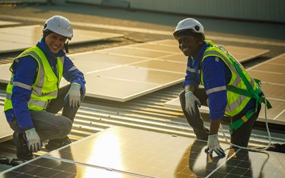 Technician performing solar panel cleaning on a rooftop with a soft brush and a water hose