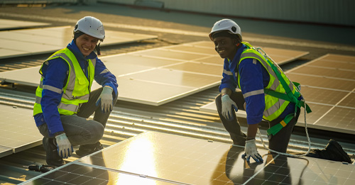 Technician performing solar panel cleaning on a rooftop with a soft brush and a water hose